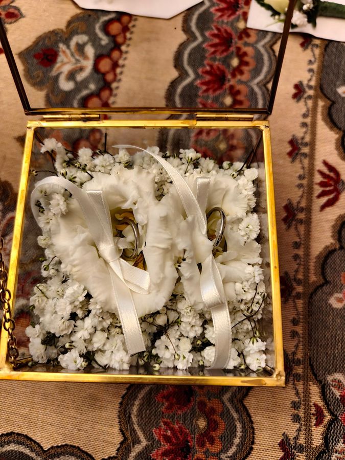 Portafedi in vetro e ottone con fedi nuziali adagiate su gypsophila e petali bianchi
