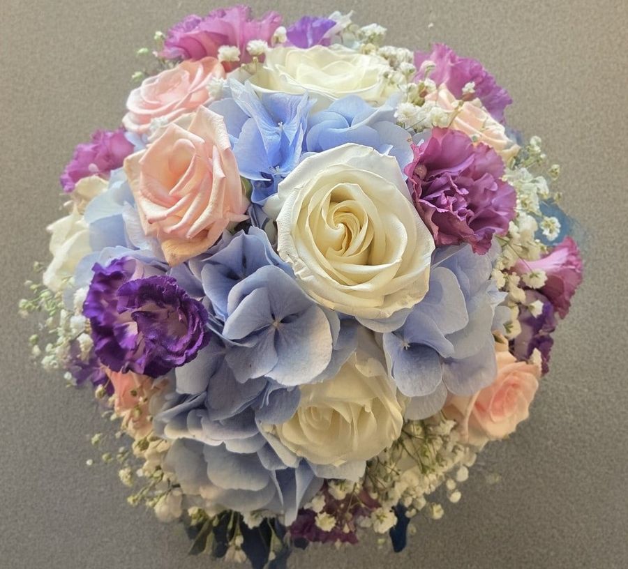 Bouquet tondo di rose bianche e pesca, ortensie azzurre, lisianthus viola e gypsophila fotografato dall'alto