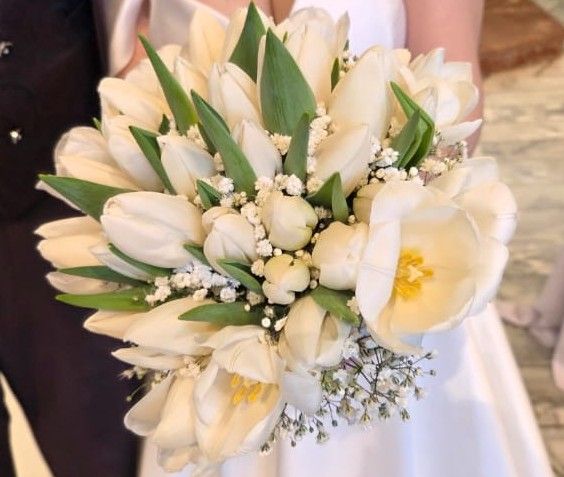 Bouquet di tulipani bianchi e nebbiolina tenuto dalla sposa davanti all'abito bianco