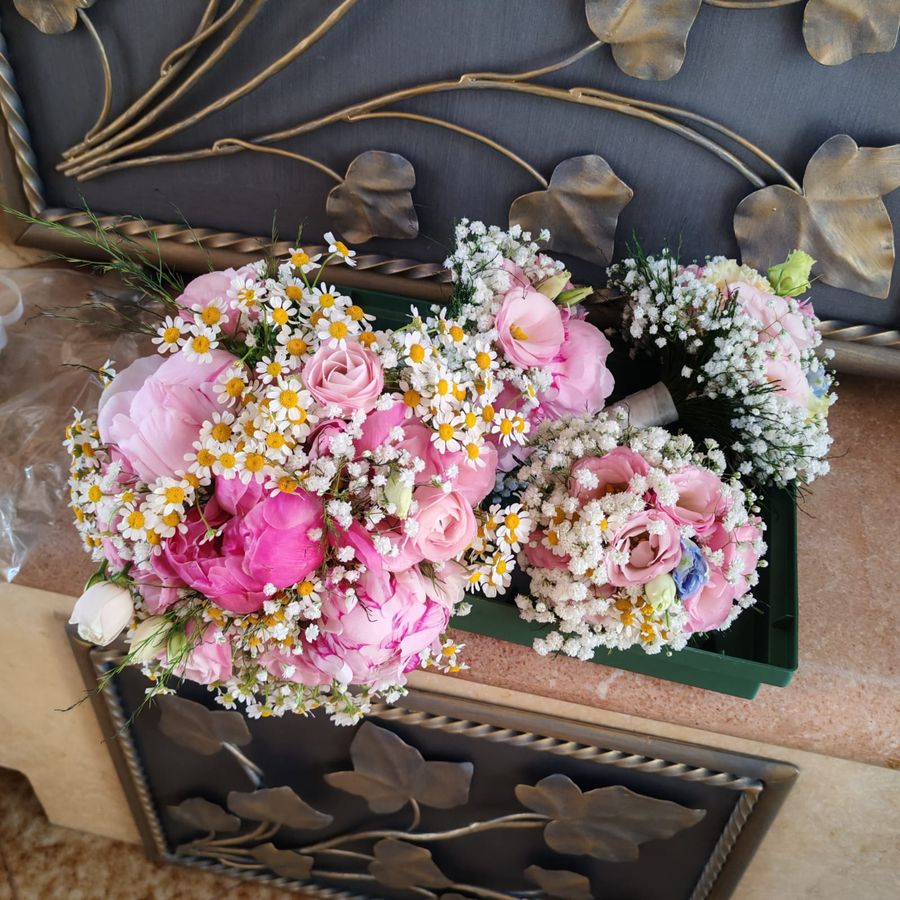 Set coordinato di bouquet da sposa e damigelle con peonie rosa, camomilla e gypsophila, pronti sul banco del laboratorio