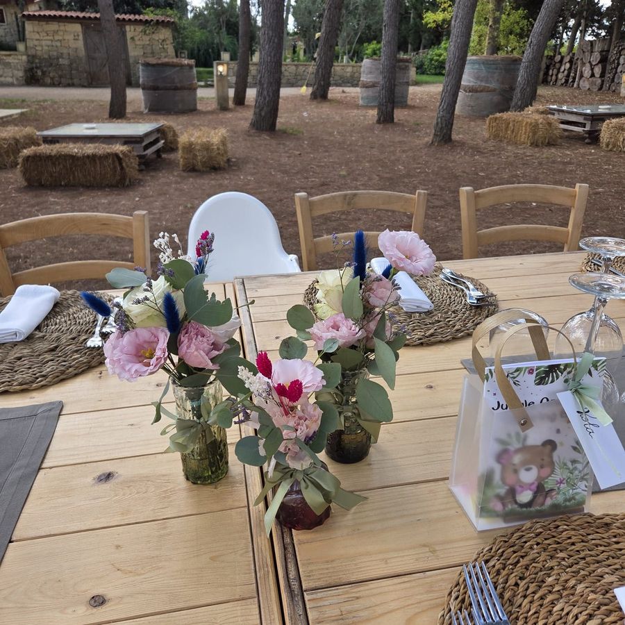 Tavolo rustico da festa all'aperto con piccoli vasi di lisianthus rosa, eucalipto e lagurus azzurro accanto alle bomboniere a tema orsetto