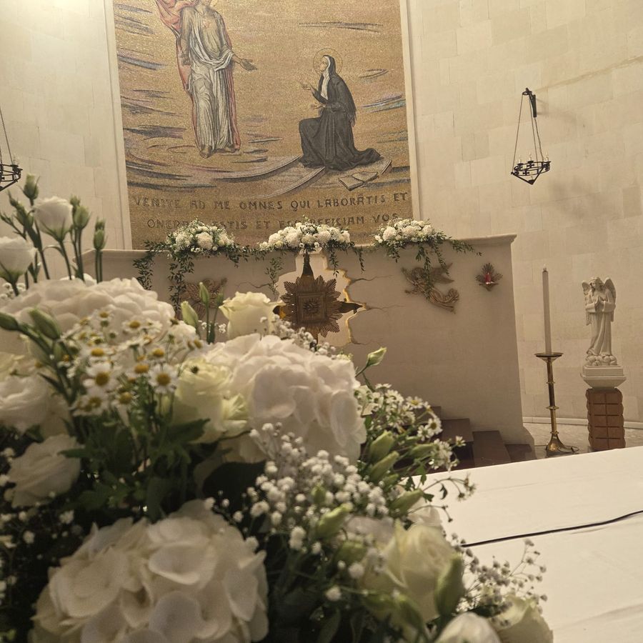 Addobbo floreale bianco sull'altare di una chiesa con ghirlande di rose e ortensie e composizione in primo piano