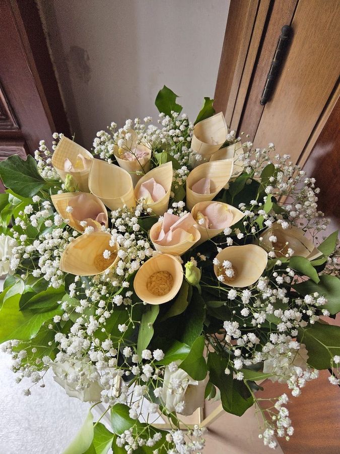 Composizione porta-riso da matrimonio con coni in legno riempiti di petali di rosa e riso, tra velo da sposa e edera