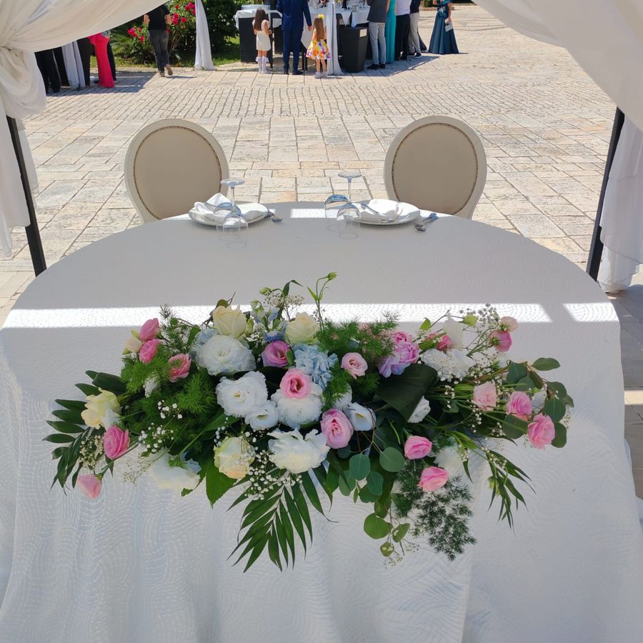 Tavolo degli sposi sotto gazebo con composizione frontale di rose rosa, lisianthus bianchi, ortensie azzurre e verde