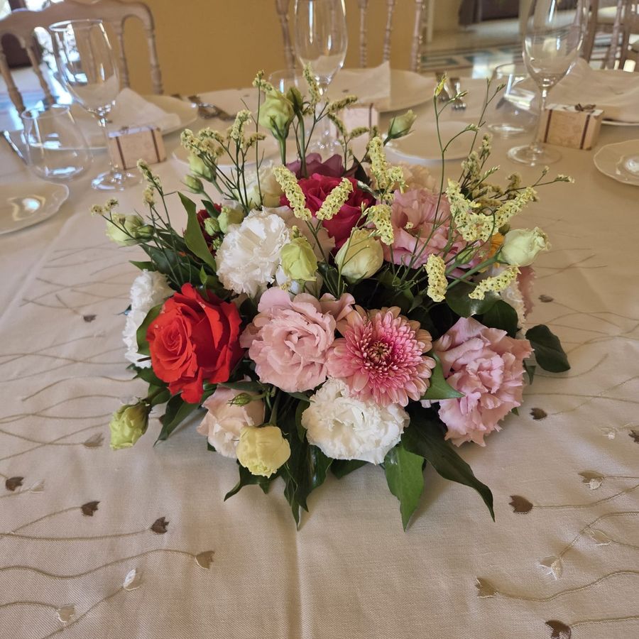 Centrotavola tondo di rose, garofani e lisianthus nei toni rosa, rosso e bianco su tavolo apparecchiato in sala ricevimento