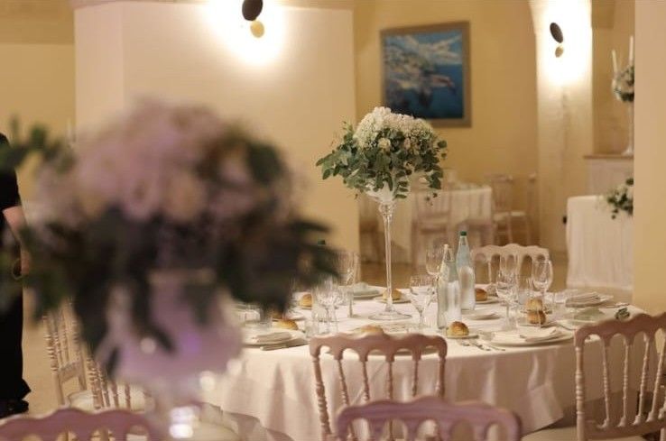Sala ricevimento con tavoli rotondi apparecchiati e centrotavola alti di fiori bianchi e verde su alzate di vetro