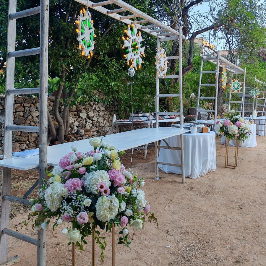 Allestimento di aperitivo in giardino con colonne floreali di ortensie rosa e bianche, rose e lisianthus sotto pergolati con luminarie